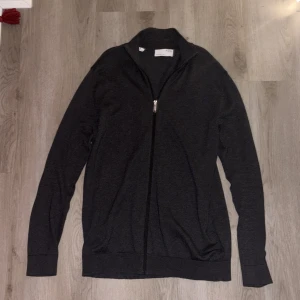 Grå tröja med dragkedja från Selected - Snygg och stilren grå tröja från Selected med dragkedja framtill. Perfekt för lager-på-lager och passar till många olika outfits. Tröjan har långa ärmar och en hög krage för extra värme. Den är knappt använd och är i ett mycket bra skick! Hör av er kring frågor!