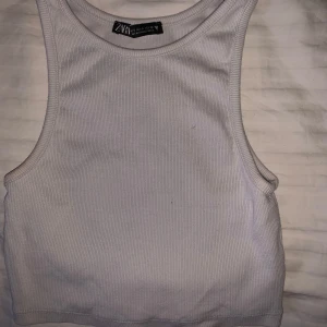 Vit ribbad linnetopp från Zara - Säljer en stilren vit ribbad linnetopp från Zara. Perfekt för varma dagar eller som ett lager under en jacka. Toppen har en klassisk design med rund halsringning.