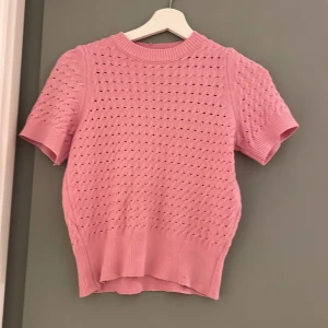 Rosa stickad tröja - Söt rosa stickad tröja med korta ärmar och ett fint hålmönster. Perfekt för vår och sommar. Den har en ribbad kant vid ärmslut och nederkant som ger en snygg passform.