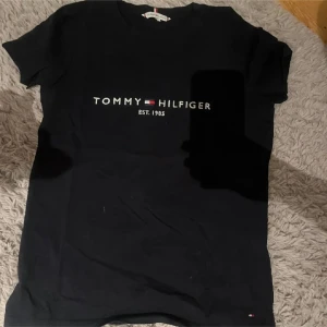 Svart t-shirt från Tommy Hilfiger - Snygg svart t-shirt från Tommy Hilfiger. Perfekt för en casual look. Klassisk passform och kortärmad design. STORLEK S MEN PASSAR EN M (knappt använd har bara hund i hemmet)