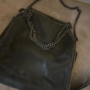 Grå väska med kedjor - Säljer denna super fina väska!, exakt som den svarta på andra bilden bara att denna då är grå. Aldrig använd.