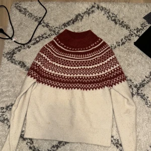 Röd och vit stickad tröja från H&M - Mysig stickad tröja från H&M i rött och vitt med ett vackert mönster runt halsen. Perfekt för kyliga dagar med sin varma och bekväma design. Tröjan har långa ärmar och en rund halsringning. Storlek XS men skulle säga att den passar även S (väldigt stretchig) 