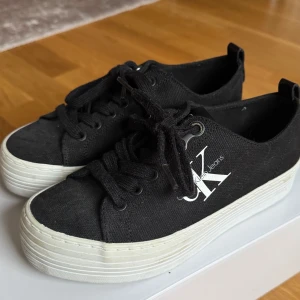 Svarta sneakers från Calvin Klein - Snygga svarta sneakers från Calvin Klein med vit sula och klassisk snörning. Perfekta för en stilren look.