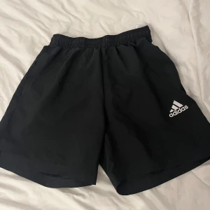 Svarta shorts från Adidas - Snygga svarta shorts från Adidas med elastisk midja och klassisk logga på benet. Perfekta för träning eller en avslappnad dag. Lätta och bekväma att bära.