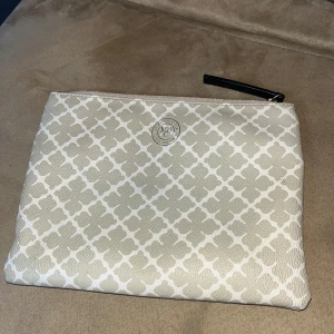 Malene Birger väska - Snygg beige kuvertväska med ett elegant rutigt mönster och dragkedja. Perfekt för att hålla dina småsaker organiserade med stil. Toppen skick och är köpt från Malene Birgers hemsida.