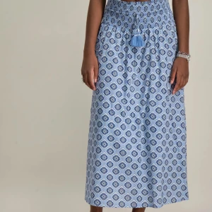 Blå mönstrad långkjol - Snygg slutsåld blå långkjol med ett unikt mönster i vitt och mörkblått. Kjolen har en elastisk midja med knytband och tofsdetalj. Perfekt för en avslappnad och stilren look. Stl 170 men passar även mindre 😛🎊💘 