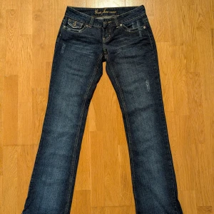 Mörkblå jeans från Guess - Snygga mörkblå jeans från Guess. Design med slitningar, en på varje bens framsida och på fickorna. Lågmidjade. Mycket fint skick. Säljer för att de inte passar längre. Innerbenslängd ca 83 cm, storlek 27 i midjan. 