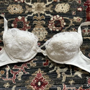 Vit spets-bh med rosett och pärldetalj! - Elegant vit bh med spetsdetaljer och en söt rosett med pärla framtill. Endast använd fåtal gånger, så i mycket bra skick! I storlek 70B! Justerbara axelband för perfekt passform. Perfekt för en romantisk look.