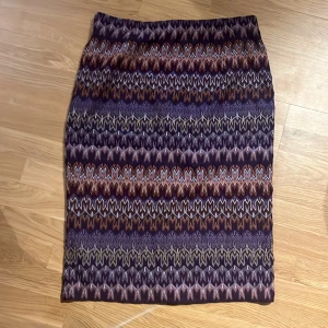 Mönstrad pennkjol från Missoni Lindex 38 - Snygg mönstrad kjol från Missoni Lindex i olika nyanser av lila, orange och beige. Kjolen har ett zigzag-mönster och en dragkedja bak. Perfekt för att ge din outfit en färgglad touch! Oanvänd