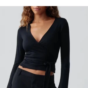 Svart omlottopp med knytband - Snygg svart omlottopp med långa ärmar och knytband i midjan. Perfekt för en stilren look. Aldrig använd slutsåld över allt