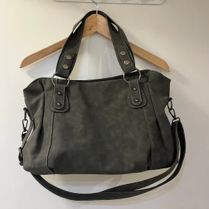 Grå/Grön axelväska med detaljer - Snygg grå/grön axelväska med justerbar axelrem och dubbla handtag. Väskan har dekorativa sömmar och metallringar som ger en cool look. Perfekt för att bära dina dagliga nödvändigheter med stil.