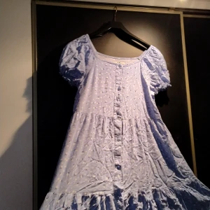 Blå klänning från Hampton Republic - Charmig ljusblå klänning från Hampton Republic med små blommor och knappar framtill. Den har korta puffärmar och en luftig passform, perfekt för varma dagar. 