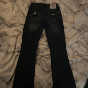 Mörkblå bootcut jeans från True Religion - Säljer ett par snygga mörkblå bootcut jeans från True Religion. De har en midwaist passform och klassiska femficksdetaljer med knappar och dragkedja. Perfekta för en stilren look!