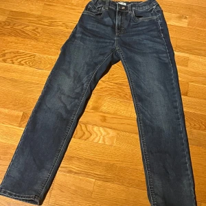 Blå jeans från Lindex - Snygga blå jeans från Lindex med klassisk femficksdesign. De har en rak passform och är tillverkade i bomull, vilket gör dem bekväma för vardagsbruk. Perfekta för en avslappnad stil.