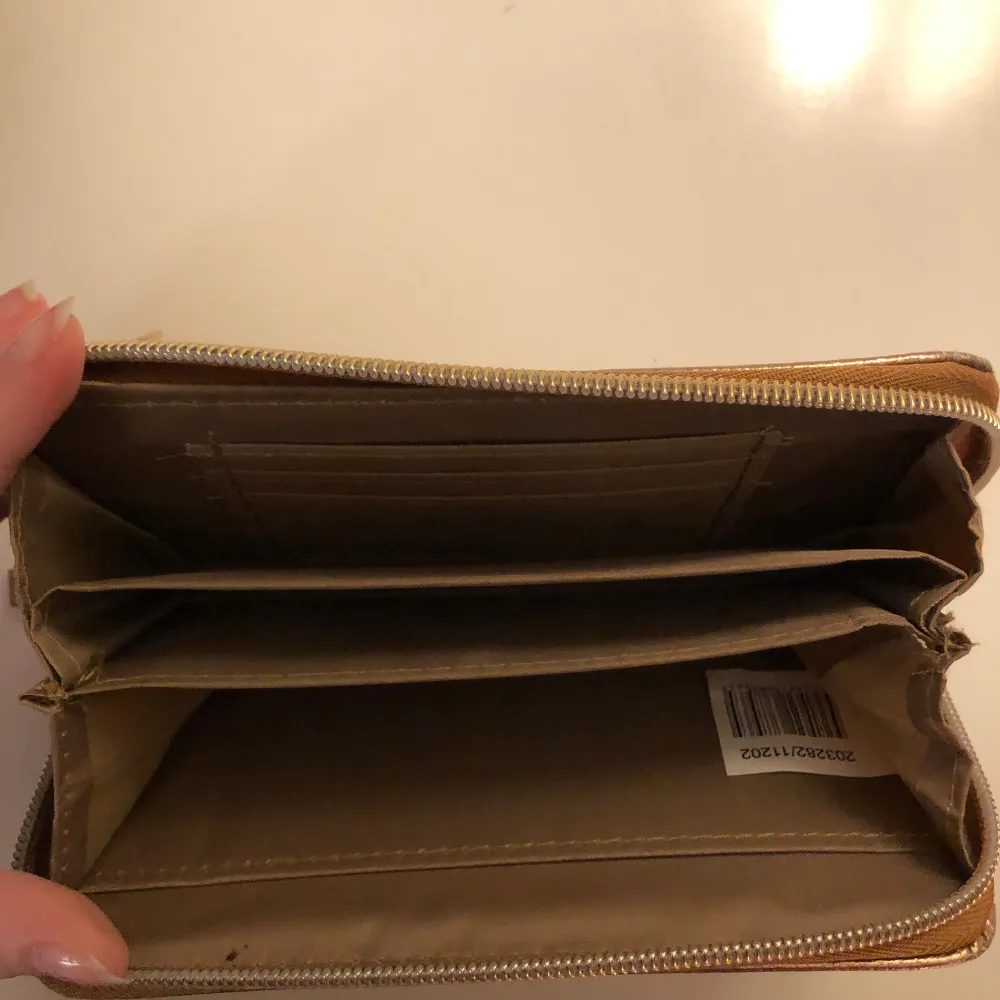 Snygg guldig plånbok med dragkedja och flera fack för kort och kontanter. Perfekt för att hålla ordning på dina tillhörigheter med stil. Märket 'STYLE' pryder framsidan.. Laukut & Käsilaukut.