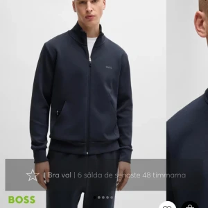 BOSS hoodie - Snygg svart hoodie från BOSS med dragkedja och hög krage. Perfekt för en stilren look. Jackan har långa ärmar och diskret logga på bröstet. Storlek m 