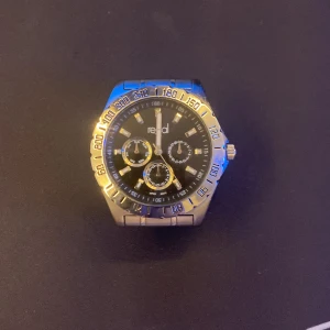 Stilren klocka från Regal - Snygg klocka från Regal med svart urtavla och silverfärgad boett. Klockan har tre små urtavlor och en guldfärgad bezel med markeringar. Armbandet är i rostfritt stål och ger en klassisk look. Perfekt för den som gillar en tidlös stil,Priset kan gå ner vid snabb affär
