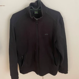 Svart jacka från Boss - Snygg svart jacka från Boss med dragkedja framtill och diskret logga på bröstet. Jackan har långa ärmar och en stilren design, perfekt för en casual look.