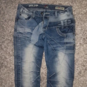 Blå straight leg jeans med detaljer från jeprag tidigt 2000  - Snygga blå jeans från Famous Denim / Jeprag med coola slitningar och nitar på bakfickan. Byxorna har flera fickor och en unik design med textdetaljer. Perfekt för en trendig look!