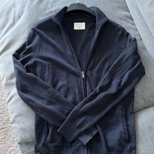 Mörkblå fullzip  - Säljer en stilren mörkblå tröja från Cortefiel med dragkedja framtill. Tröjan har långa ärmar och ribbade muddar vid ärmslut och nederkant. Perfekt för en avslappnad look. 