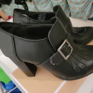 Svarta boots med spänne - Snygga svarta boots med en dekorativ spänne och fransdetalj framtill. Perfekta för en stilren look med en liten klack för extra höjd. Från Zanlando.