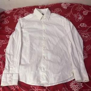 Vit skjorta från H&M - Klassisk vit skjorta från H&M i storlek M. Skjortan har långa ärmar och knappar framtill. Perfekt för en stilren look.