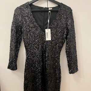 Svart paljettklänning från NLY Trend - Snygg svart paljettklänning från NLY Trend med v-ringning och trekvartsärmar. Perfekt för en glittrig kväll med stil. Klänningen har en dragkedja i ryggen