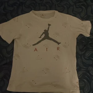 Vit t-shirt med Air Jordan-tryck - Säljer en vit t-shirt från Jordan med det ikoniska Air Jordan-trycket i svart och rött på framsidan. T-shirten har korta ärmar och är perfekt för en sportig look.