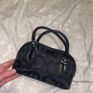 Svart handväska - Snygg svart handväska med diskret mönster och två handtag. Väskan har en dragkedja upptill och är perfekt för att bära med sig det viktigaste. Stilren och enkel design som passar till många tillfällen.