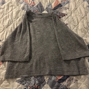 Grå stickad tröja - Mysig grå stickad tröja med trekvartsärm. Perfekt för kyliga dagar och enkel att matcha med olika outfits.