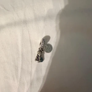 Silverberlock från Pandora - Charmig silverberlock från Pandora med två hängande detaljer: motiv av mulan i ett samarbete med Disney, hängande berlock säger ”be strong and be yourself”.