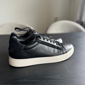 Svarta sneakers från Calvin Klein - Snygga svarta sneakers från Calvin Klein i skinn med vit sula. Skorna har klassisk snörning och en stilren design som passar perfekt till vardags!   Använda 2 gånger 