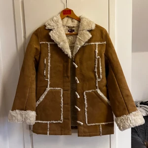 Brun shearling jacka - Säljer en supersnygg brun shearlingjacka med vitt foder och dekorativa sömmar. Jackan har långa ärmar och stängs med knappar framtill. Köpte den secondhand men den är i nyskick🌟🌟