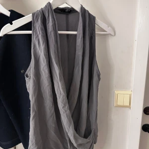 Grå ärmlös topp från Filippa K - Säljer en stilren grå ärmlös topp från Filippa K. Toppen har en draperad design framtill som ger en elegant look. Perfekt för att klä upp eller ner beroende på tillfälle. Skulle säga att den passar S-M och inte L, fler bilder går att få