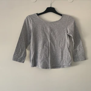 Grå tröja från H&M - Säljer en stilren grå tröja från H&M med trekvartsärmar och en snygg snörning i ryggen. Perfekt för en avslappnad look. Tröjan är i mjukt material och har en normal passform. Passar bra till både jeans och kjol.