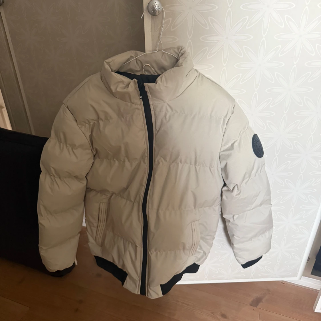 Grå pufferjacka med svart emblem