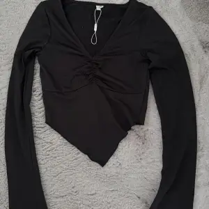 Snygg svart långärmad topp med v-ringning och rynkdetalj framtill. Perfekt för en stilren look. Aldrig använd 