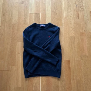 Mörkblå tröja från Morris - Säljer en stilren mörkblå tröja från Morris i 100% merinoull. Tröjan har en liten röd broderad detalj på bröstet och ribbade muddar vid ärmslut och nederkant. Perfekt för kyligare dagar! Säljer denna tröja eftersom att jag råkade krympa tröjan i tvätten. Storleken är markerad som S men sitter mer som en XS. Tveka inte att ställa frågor!