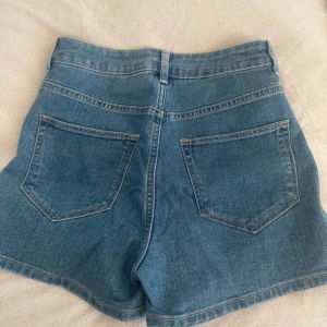Blå jeansshorts från &Denim - Snygga blå jeansshorts från &Denim med hög midja. Klassisk femficksdesign och knappgylf. Perfekta för en avslappnad stil.