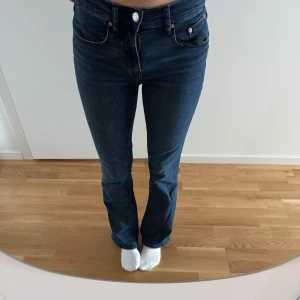 Mörkblå jeans med bootcut - Snygga mörkblå jeans med bootcut-stil och låg midja. Klassisk design med fem fickor och knappgylf. Perfekta för en avslappnad look.