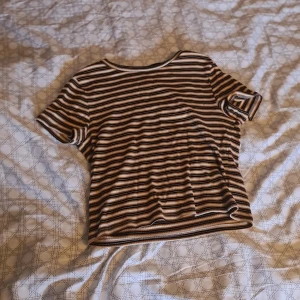 Randig t-shirt från H&M Divided - Säljer en randig t-shirt från H&M Divided i svart, vit och orange. T-shirten har korta ärmar och är ribbad vilket ger en skön passform. Perfekt för en avslappnad stil. Strl M men borde passa S också.