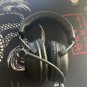 Svarta HyperX hörlurar med mikrofon - Säljer ett par svarta HyperX hörlurar med inbyggd mikrofon. De har en vadderad huvudbygel och mjuka öronkuddar för extra komfort. Perfekt för gaming eller musiklyssning.
