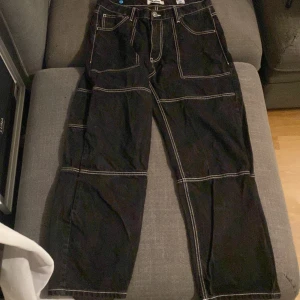 Svarta byxor med kontrastsömmar - Snygga svarta byxor med vita kontrastsömmar och flera fickor. Byxorna har en loose passform och är perfekta för en avslappnad stil. Tillverkade i Bangladesh. Har haft på mig dom typ 3 gånger så bra skick 