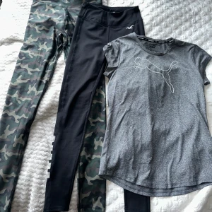 Träningskläder - Två par leggings, ett i camouflagemönster och ett svart med unika sidodetaljer från Hollister, stl xs på båda. Perfekta för träning eller en avslappnad dag. En träningströja från Puma i stl M. 100kr för alla tre plagg