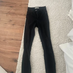Svarta skinny jeans - Snygga svarta skinny jeans med hög midja och knappar framtill. Perfekta för en stilren look och passar till det mesta. De är tillverkade i ett stretchigt material för bästa komfort.