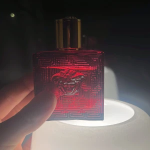 Versace Eros Flame Eau de Parfum - Säljer en elegant Versace Eros Flame Eau de Parfum i en djärv röd flaska med guldlock. Flaskan har ett intrikat mönster och den ikoniska Medusa-loggan. Perfekt för den som vill ha en doft med karaktär och stil.