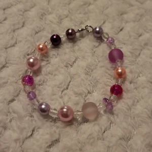 Färgglatt armband med pärlor - Charmigt armband med en mix av färgglada pärlor i rosa, lila och genomskinliga nyanser. Perfekt för att ge en färgklick till din outfit. Armbandet har en enkel låsning och är lätt att bära.