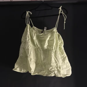 Ljusgrön linnetopp från H&M Divided - Säljer en ljusgrön linnetopp från H&M Divided med justerbara axelband. Toppen har en luftig passform och volangdetaljer som ger en söt look. Perfekt för varma dagar!