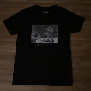 Svart t-shirt med tryck från Mister Tee - Snygg svart t-shirt från Mister Tee med ett coolt tryck av en boxningsscen och texten 'It's Goin' Down'. Perfekt för en avslappnad stil.