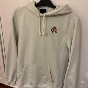Mintgröna  hoodie från H&M med rosdetalj - Säljer en mintgrön hoodie från H&M i regular fit. Den har en broderad rosdetalj på bröstet och en praktisk magficka. Perfekt för en avslappnad stil. Huvan har dragsko för justering.